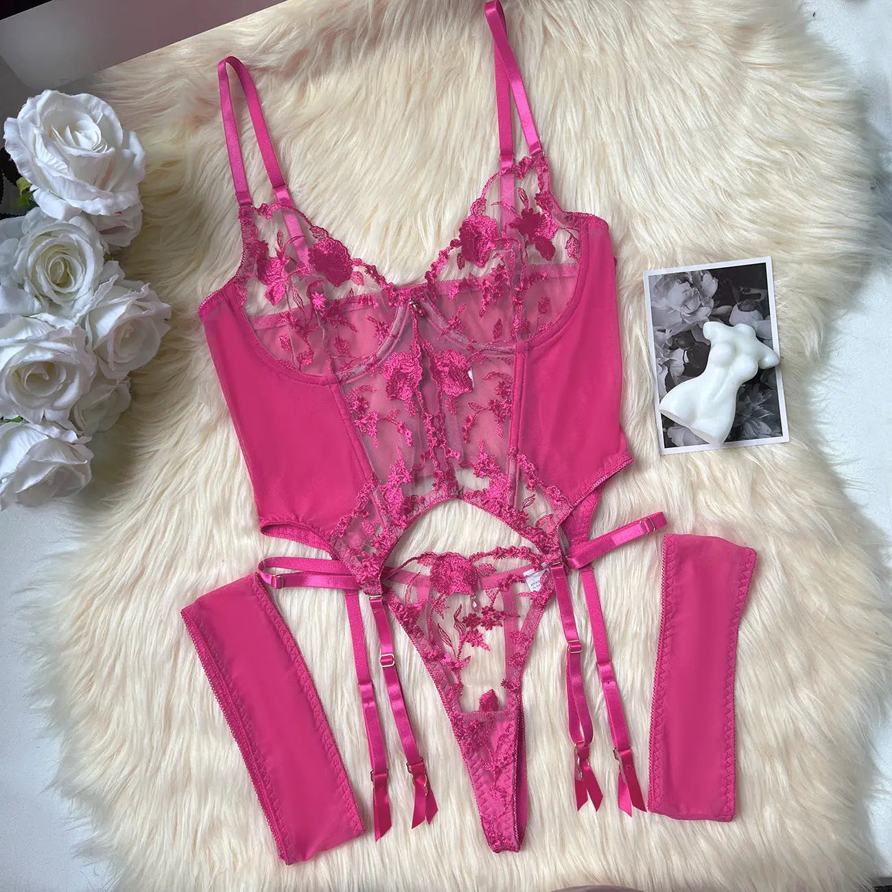Pink lace lingerie set on a fluffy white surface with flowers and a photo in the background.
