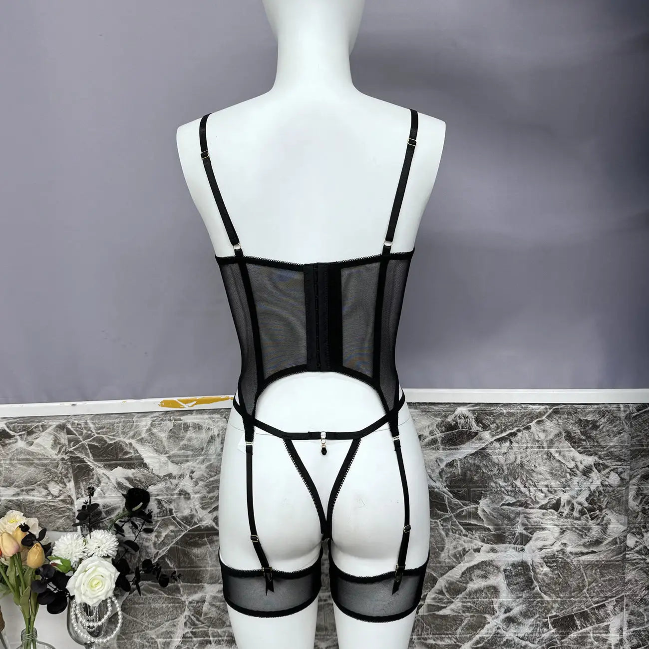 Black strappy lingerie set on a mannequin against a gray background