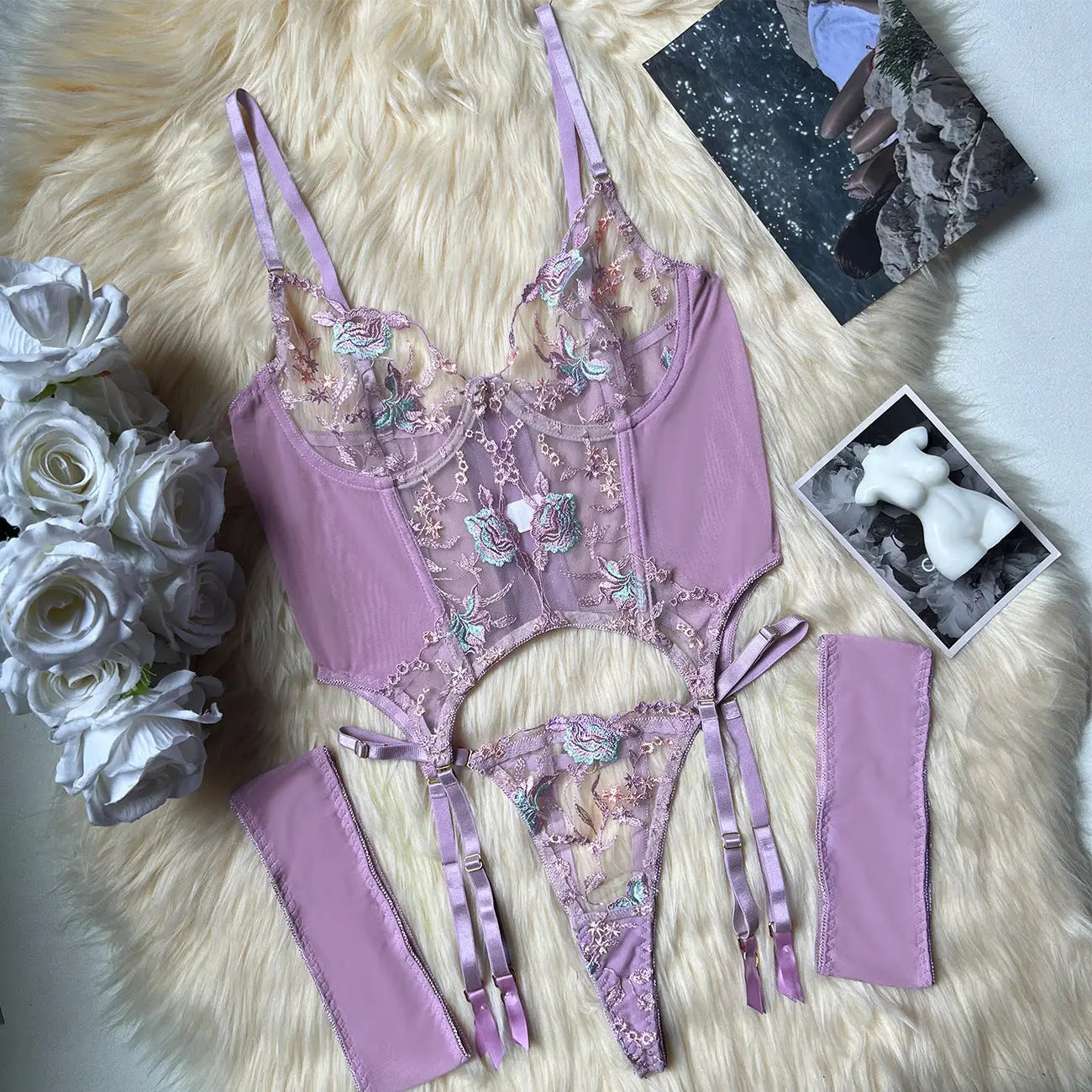 Purple lingerie set with floral details on a fluffy white surface with flowers and photos.