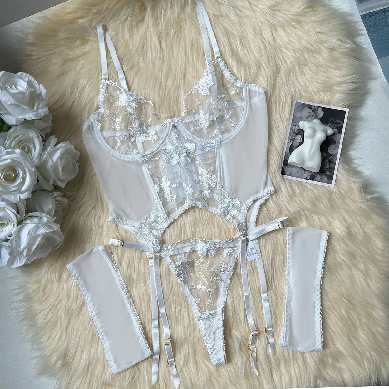 Set of lace lingerie on a fluffy surface with flowers and a photo of a mannequin.