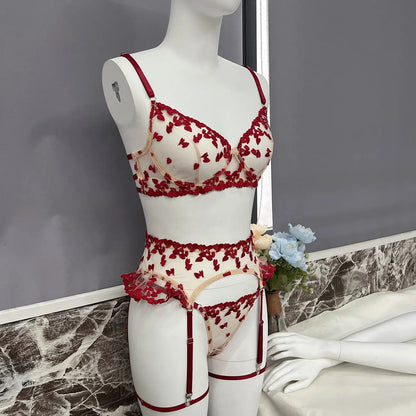 Sheer white lingerie set with red heart embroidery on a mannequin. It includes a bra, garter belt with ruffles, and thong, all featuring red straps and trim.