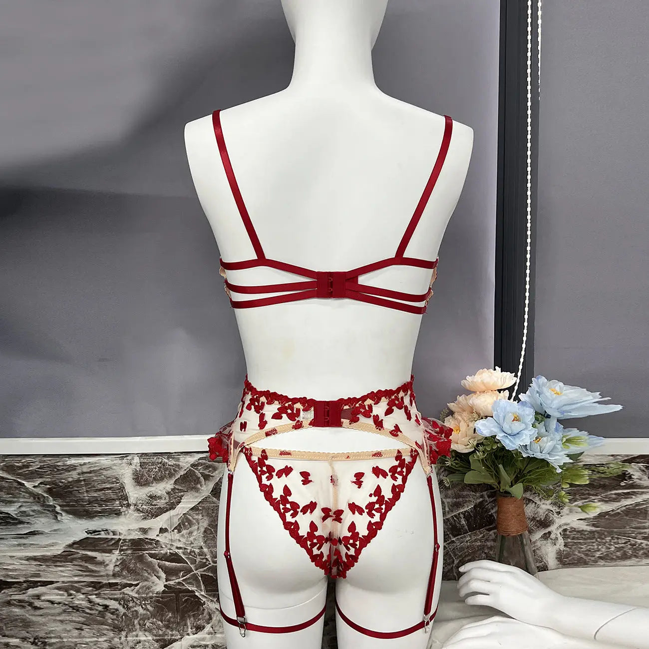 This is a luxurious red lingerie set featuring sheer fabric with delicate floral embroidery. It includes a multi-strap bra, a high-waisted garter belt with suspenders, and matching thong briefs, all adorned with intricate red detailing.