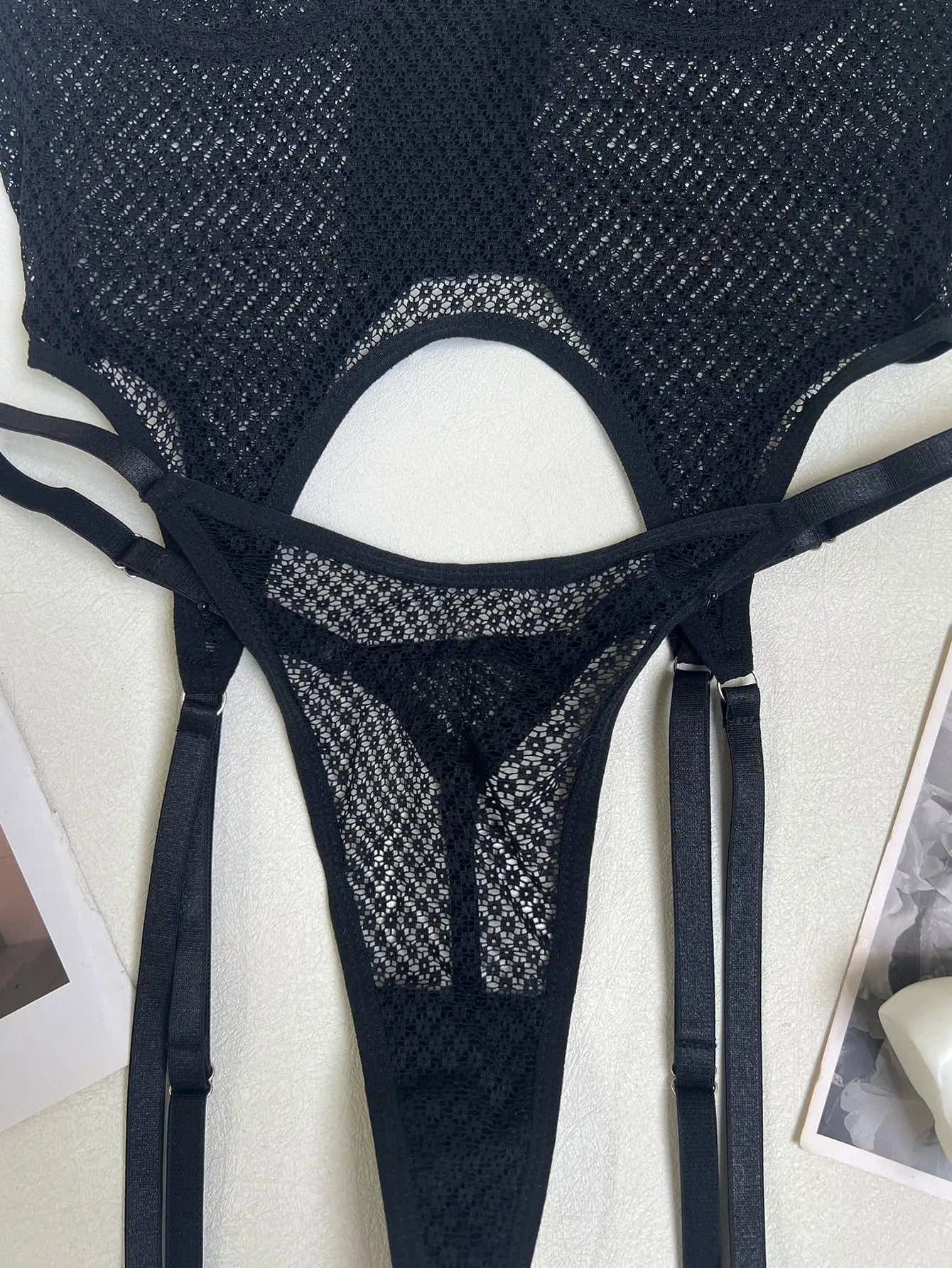A black sheer mesh lingerie set, featuring a top with a cut-out detail and a thong-style bottom with adjustable garter straps, creating an alluring look.