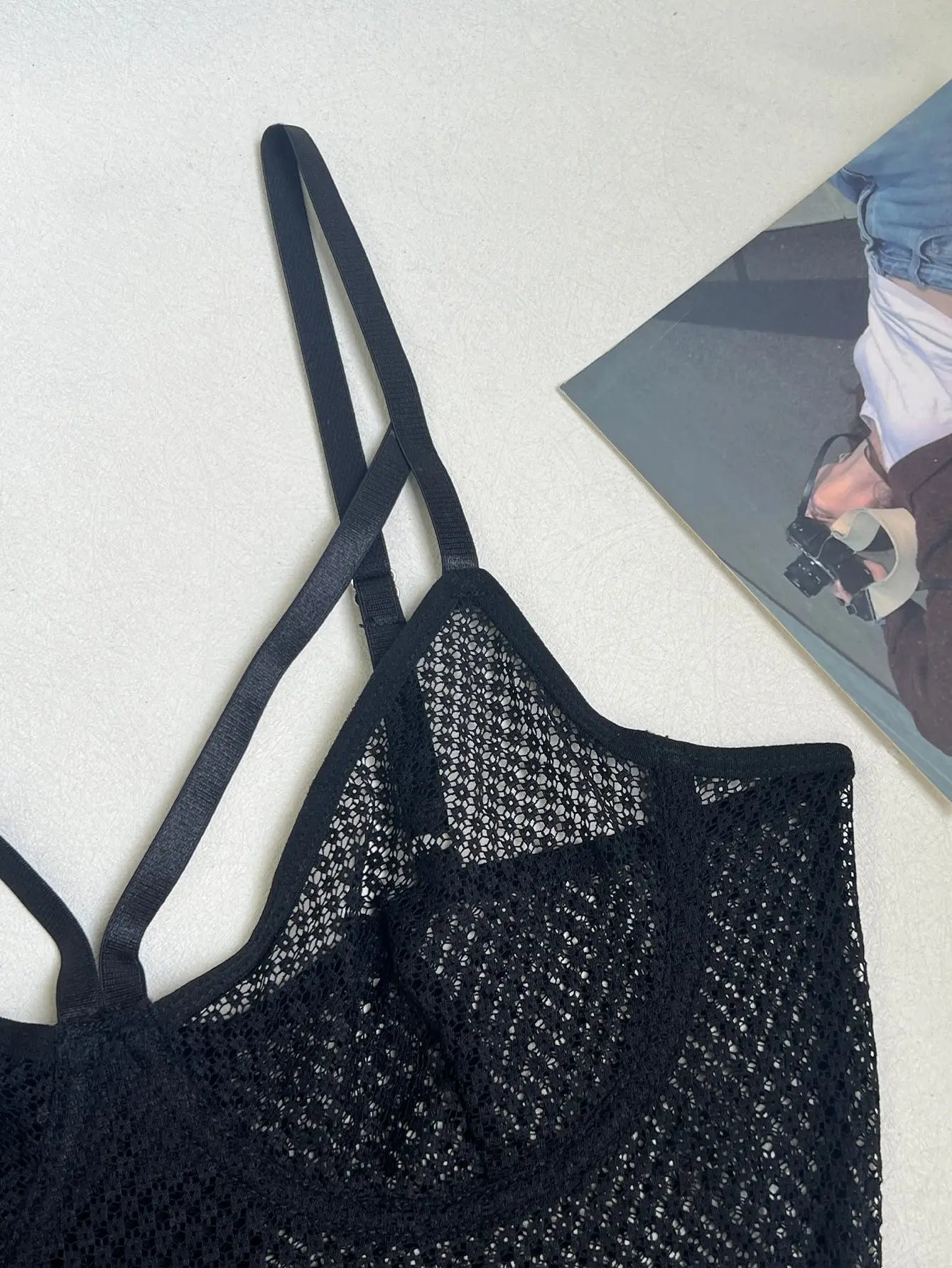 A black mesh bralette or camisole top with intricate open-weave fabric and multiple thin, adjustable straps. It features a visible bust line, suggesting inner support or shaping.