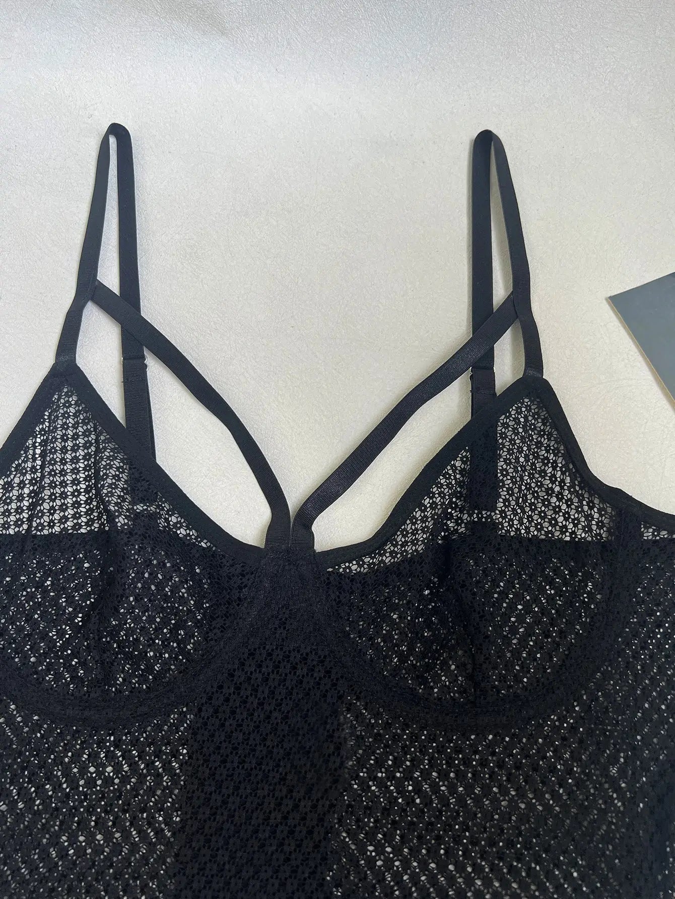 A black mesh-knit bralette or camisole featuring intricate crisscrossing straps and a sheer, open-weave design, offering a stylish and alluring look.
