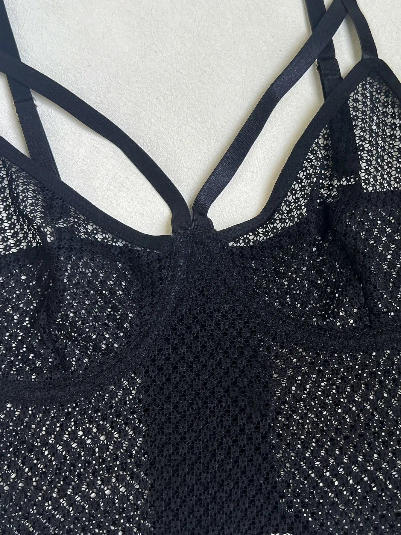 A black lace bralette or camisole top with intricate open-knit mesh detailing and multiple thin, adjustable straps. It features a delicate, semi-sheer design.