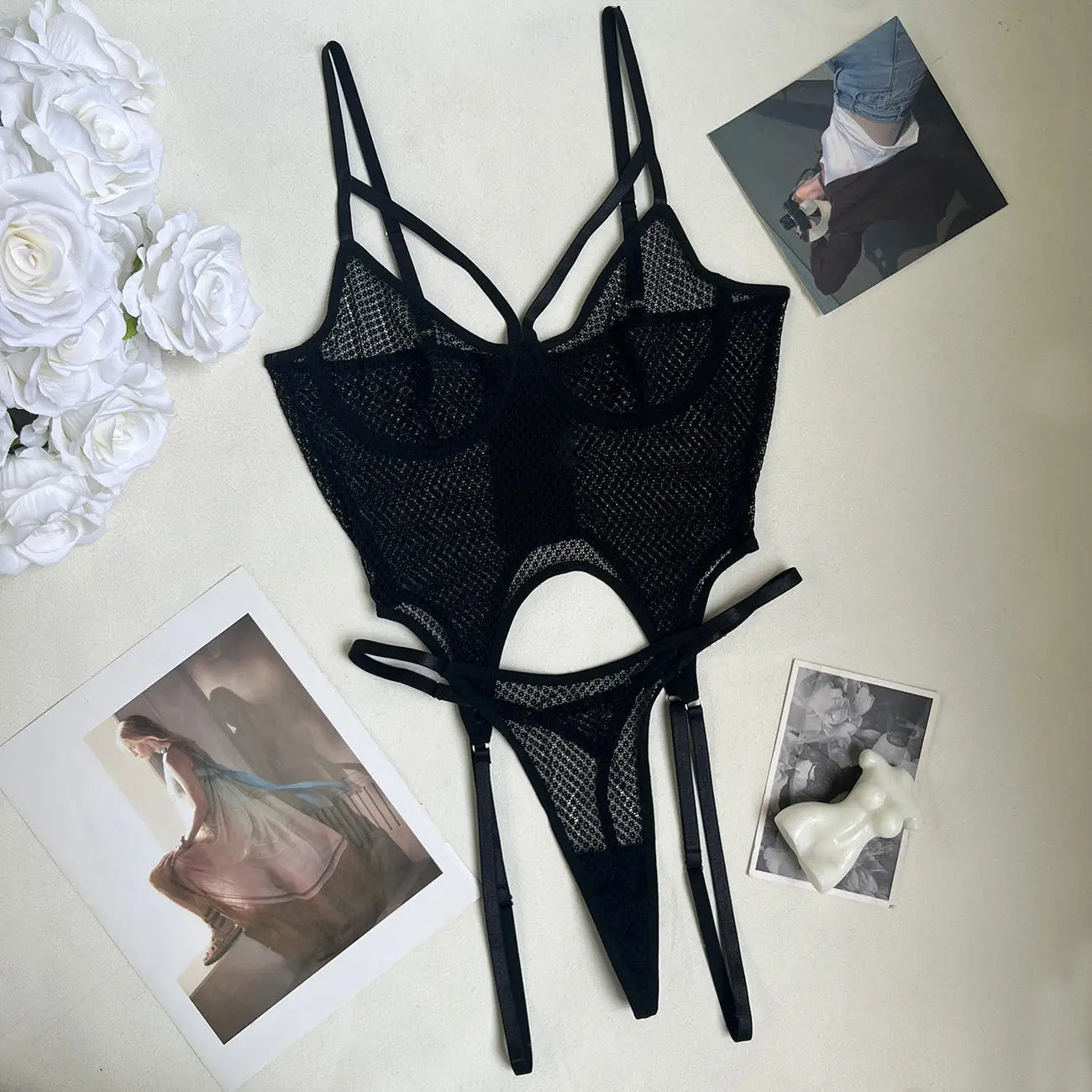 A provocative black mesh lingerie bodysuit with intricate strap details, a cut-out midsection, and integrated garter straps.