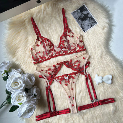 This elegant lingerie set includes a sheer nude bra, matching thong, and garter belt, all adorned with delicate red heart embroidery.