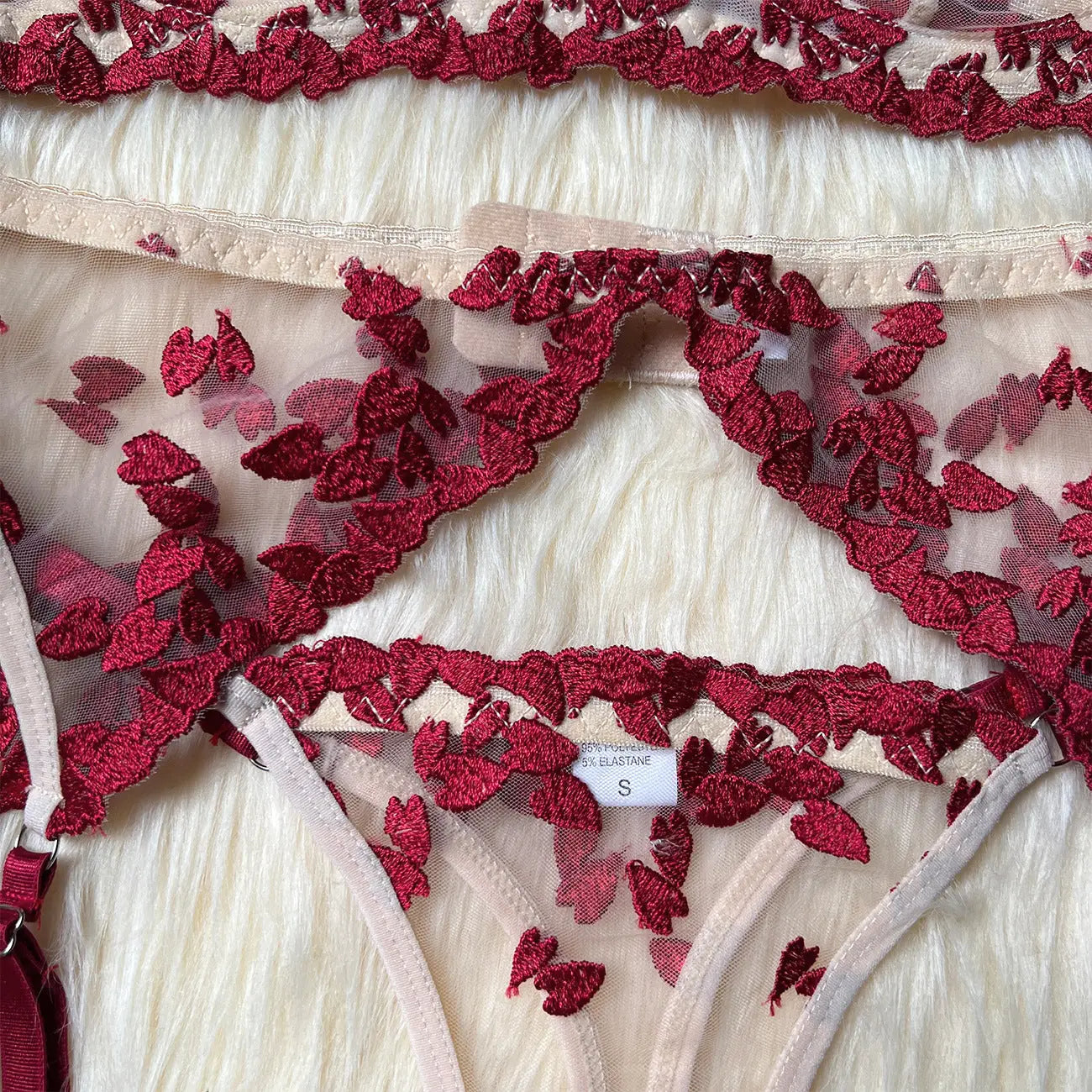 A delicate lingerie set featuring sheer nude mesh fabric adorned with intricate red embroidered floral patterns, with elements of a bra and underwear visible, displaying a 'size S' label.
