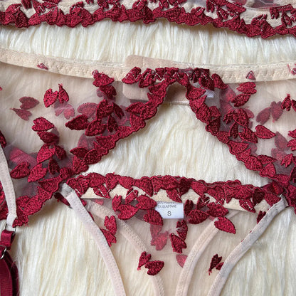A delicate lingerie set featuring sheer nude mesh fabric adorned with intricate red embroidered floral patterns, with elements of a bra and underwear visible, displaying a 'size S' label.