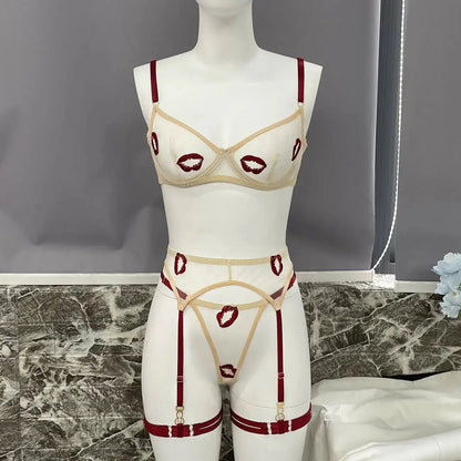 A cream sheer lingerie set featuring red lip embroidery, bra, thong, and garter belt with dark red straps, displayed on a mannequin.