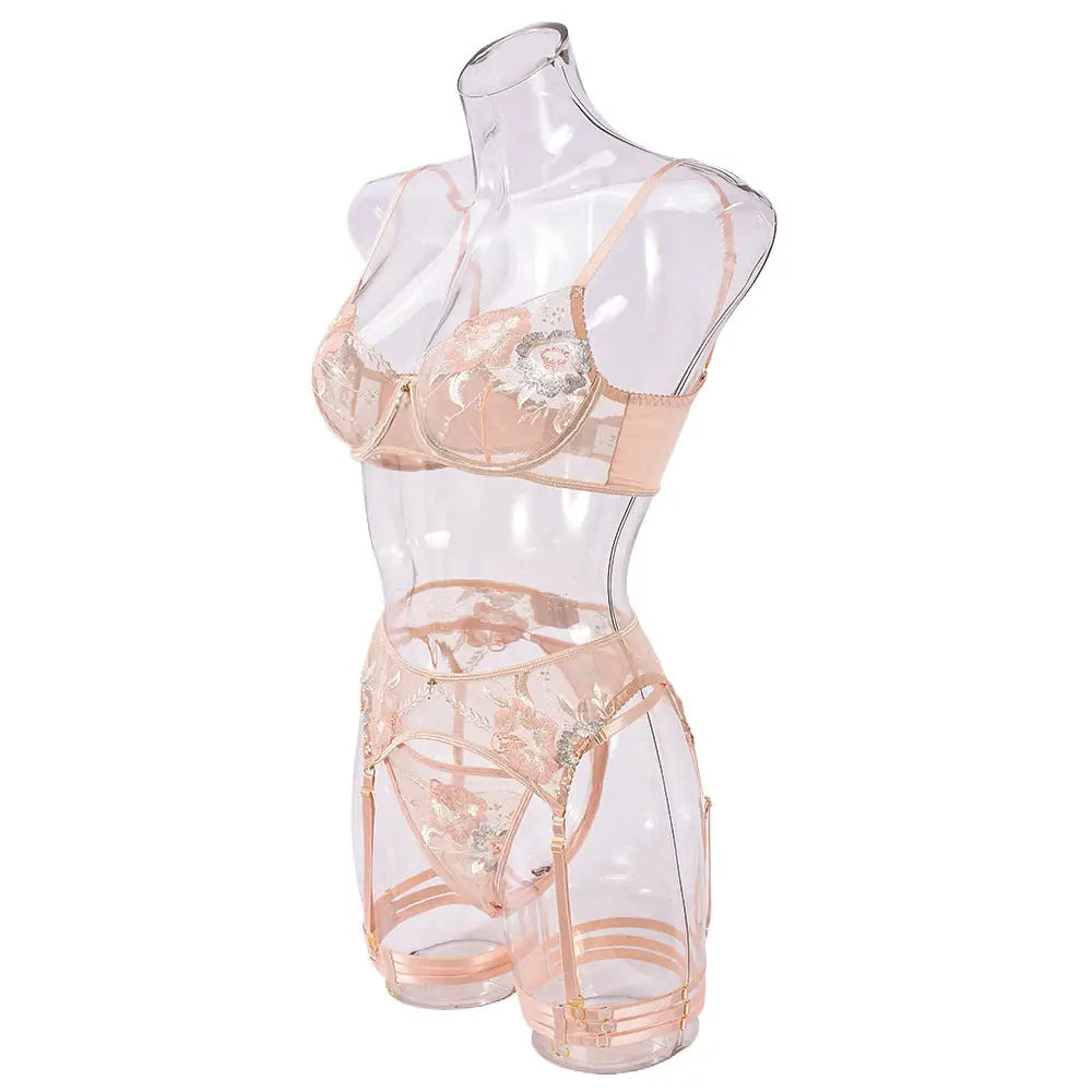 A delicate peach-colored lingerie set, featuring an embroidered bra, thong, and garter belt with intricate floral patterns, displayed on a transparent mannequin.